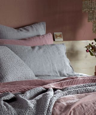 Pink and gray sheets and blankets on a bed against a pink wall.