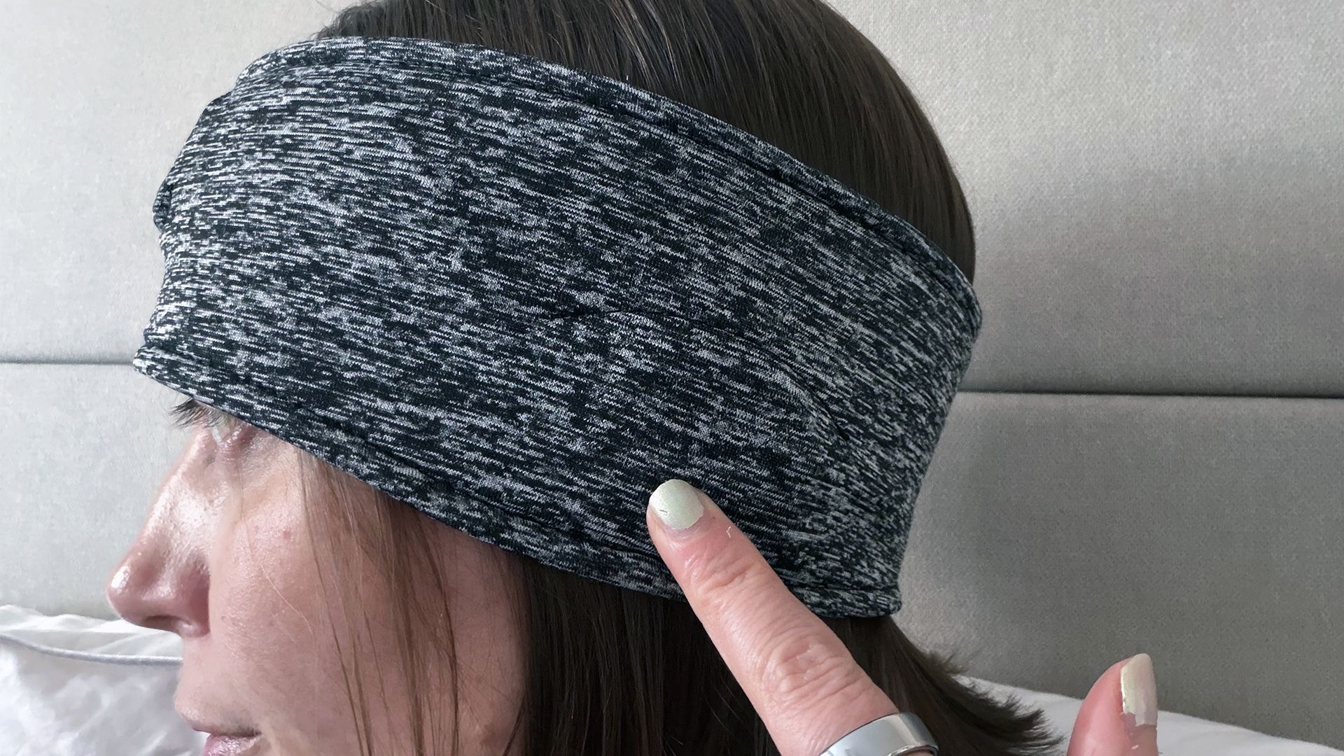 A close up of our reviewer wearing the Snoozeband with her head turned to the side. She's pointing at where the speaker sits