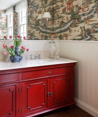 A red vanity unit in a powder room with patterned wallpaper