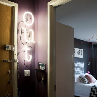 A purple-painted hallway with a neon sign next to the entrance spelling 'out'