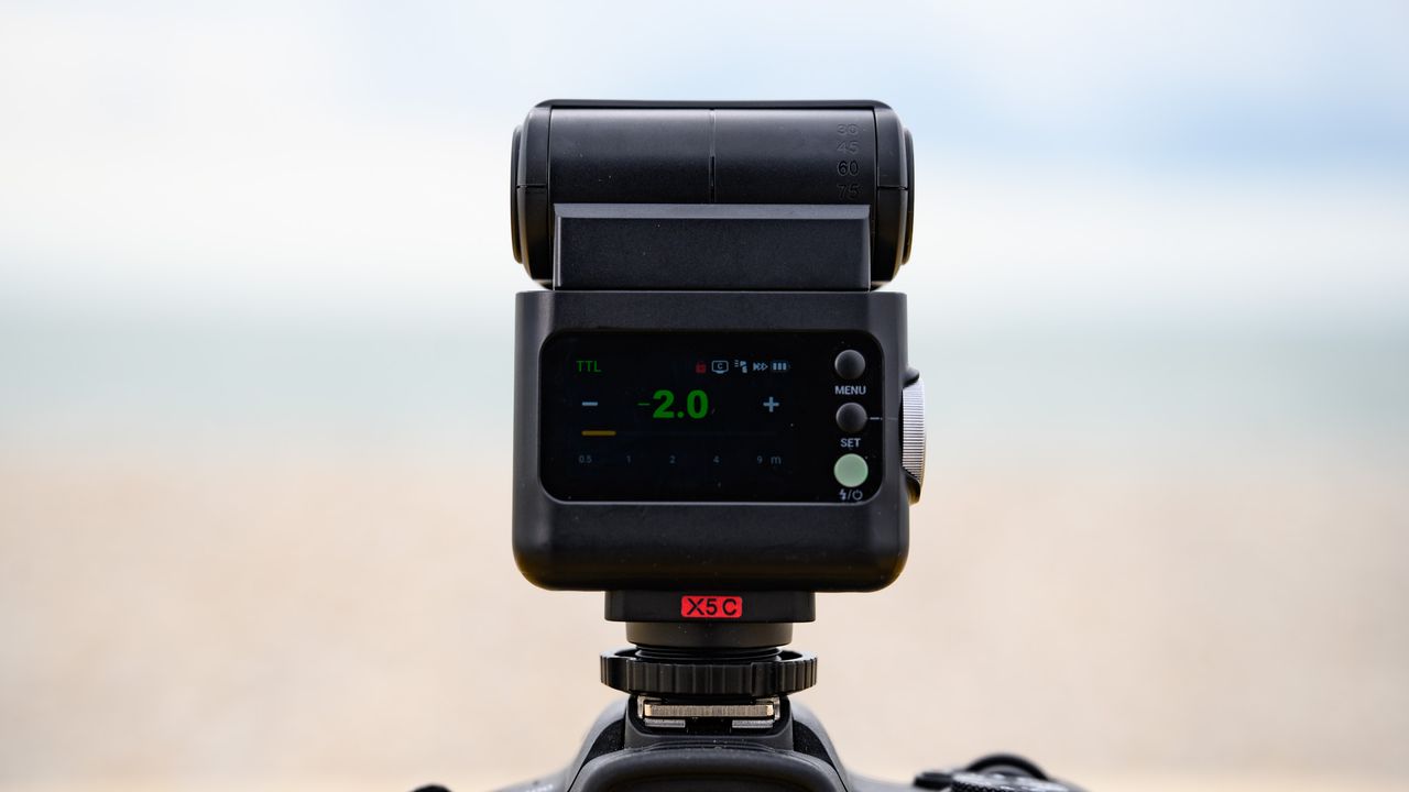 Closeup of the Godox iT32 camera flash and its rear display, the ocean is behind it