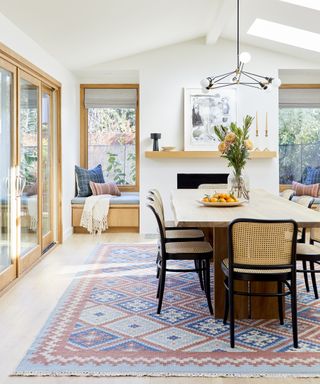 A white dining room with vaulted ceiling, large wooden dining table, blue and red rug and large glass bi-fold doors