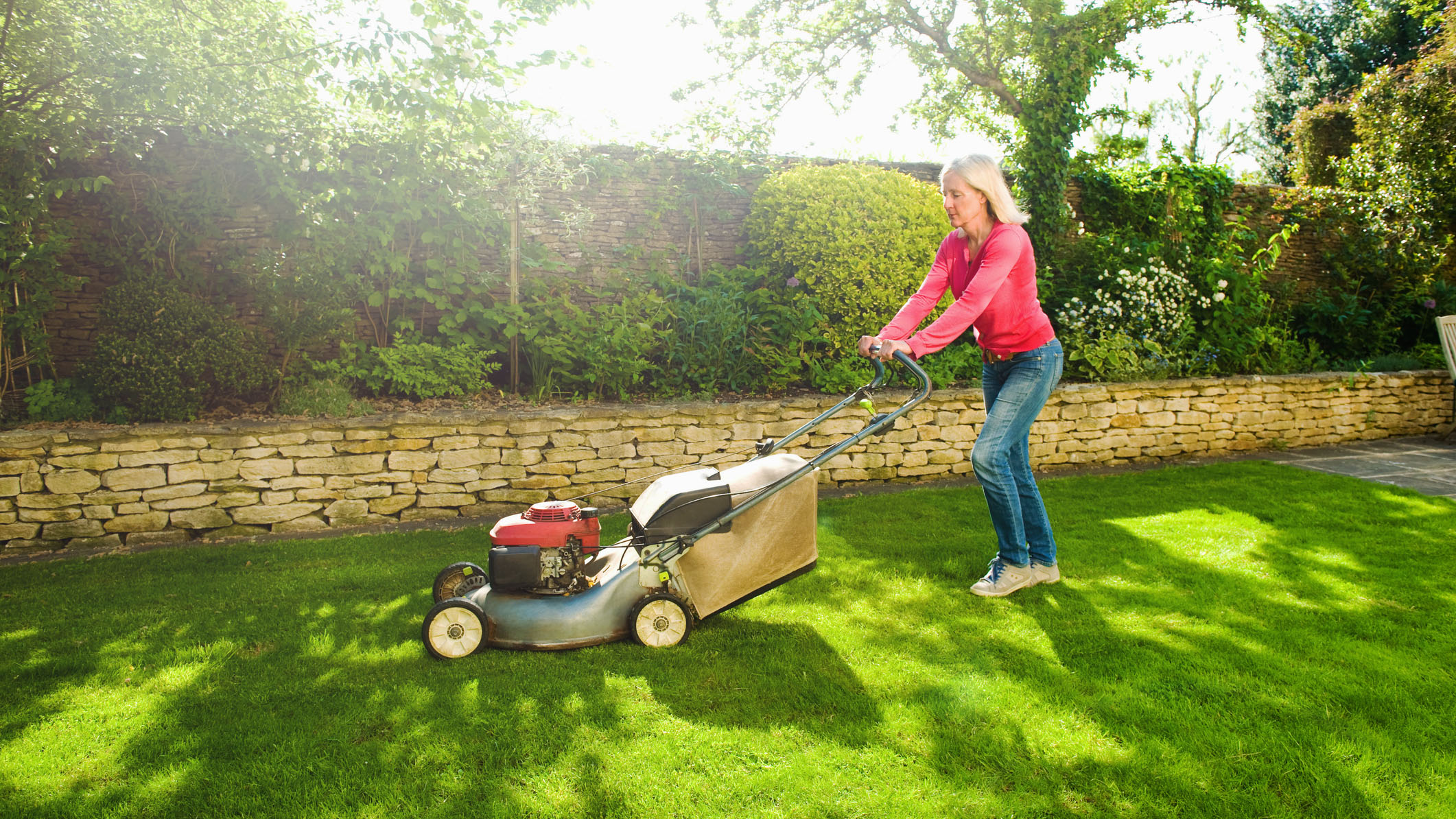 What to do if your lawn mower won't start: A woman wearing a red top uses a lawn mower to cut the grass on a sunny day