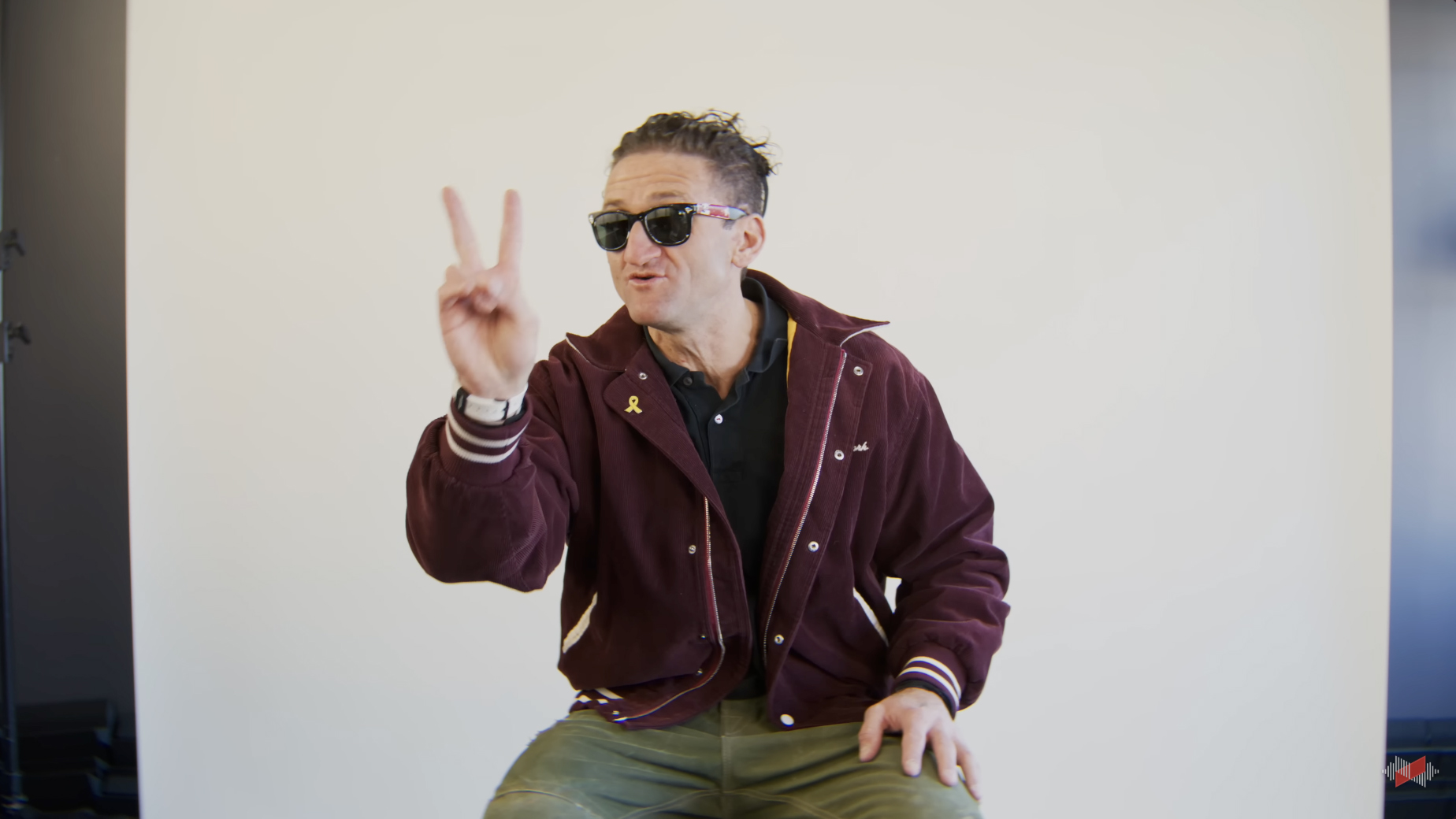 Casey Neistat, appearing on the WVFRM Podcast, sitting in front of a white backdrop holding two fingers in the air