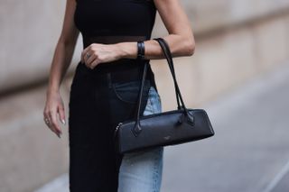 a woman walking down the street wearing a sleeveless top with jeans and an east west bag