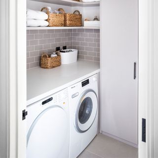 White utility room with white tumble dryer and washing machine, and grey tiles on the wall