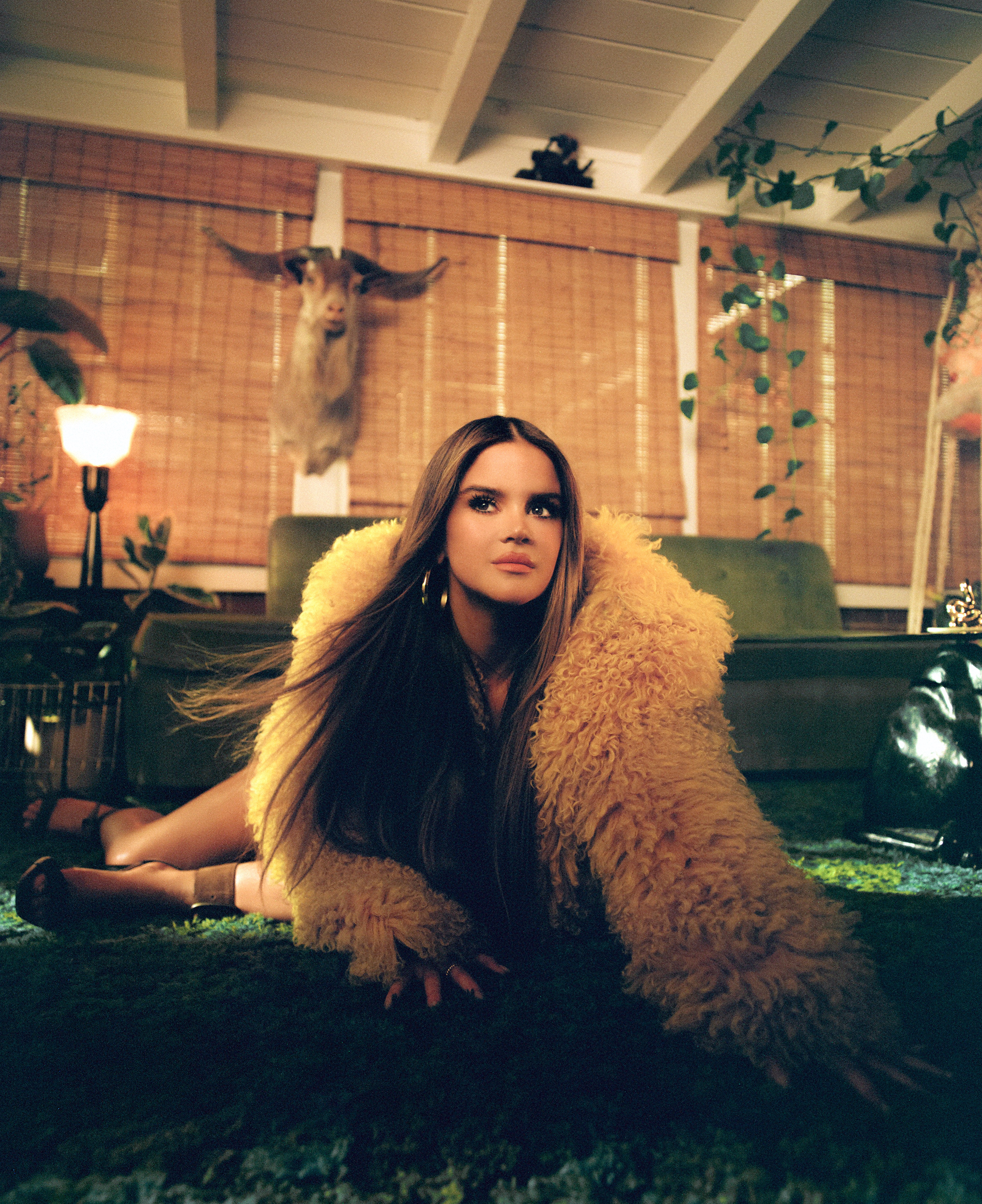 maren morris sits on the floor of a mid century modern looking living room posing and wearing a yellow fur coat