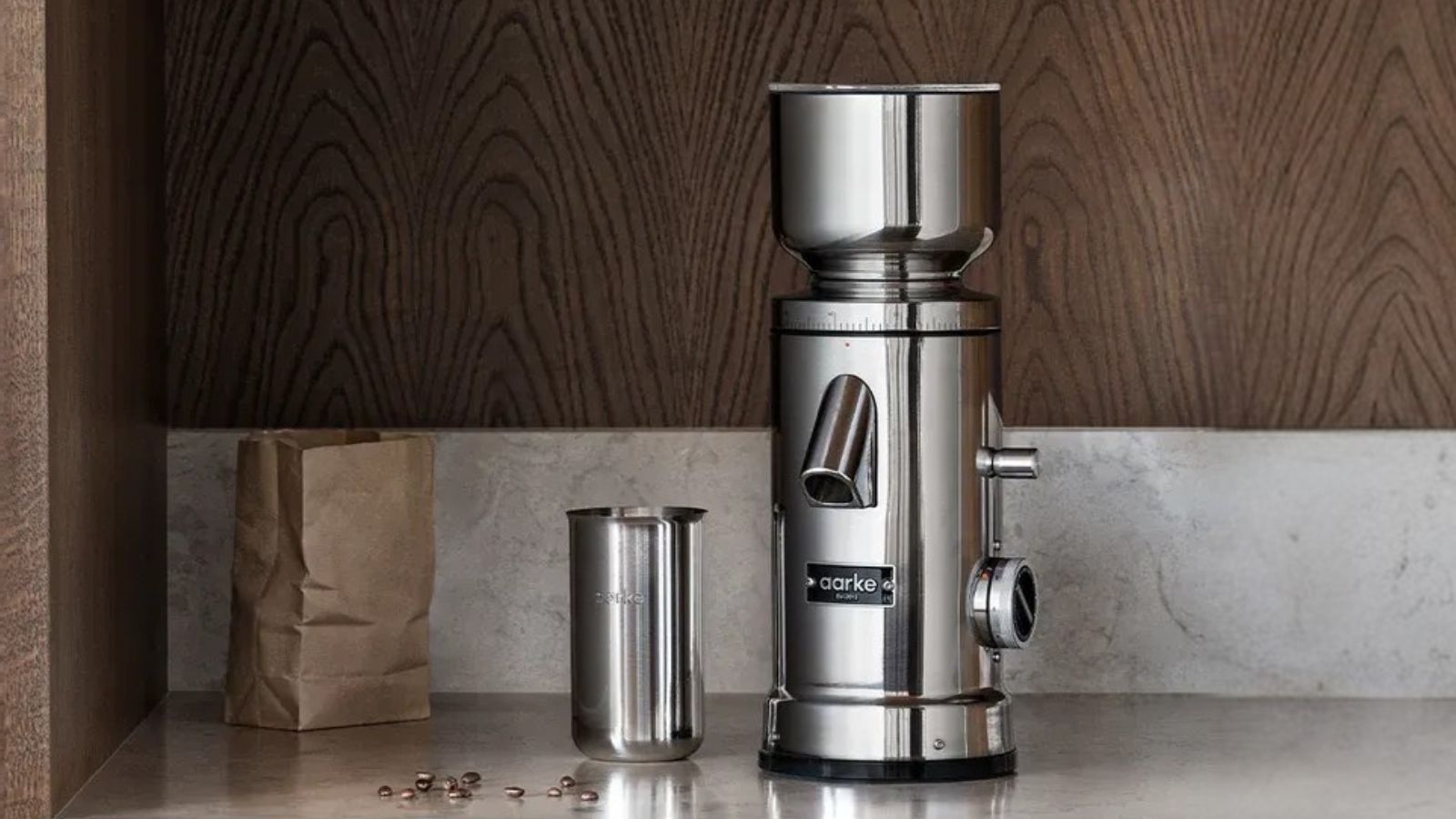 A stainless steel coffee grinder on a grinder on a marble counter with a wooden backsplash.