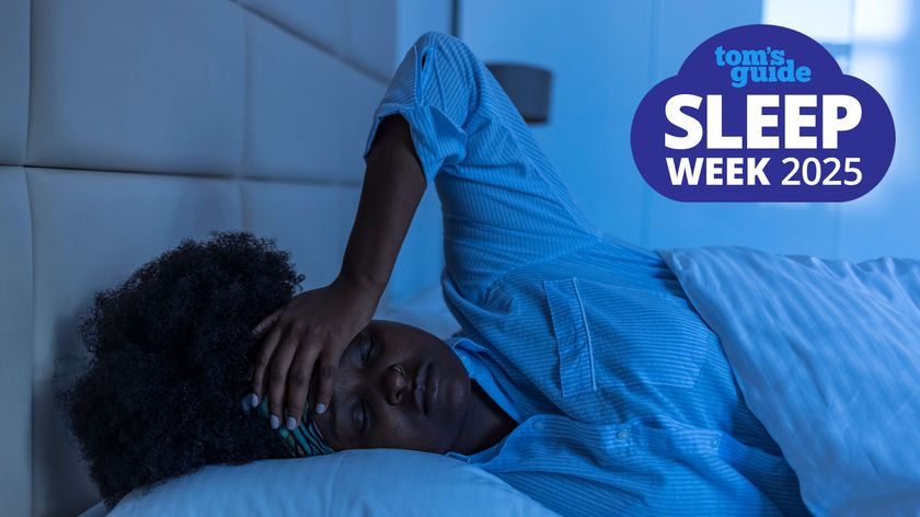 A woman with dark curly hair holds her hand to her forehead in frustration because she cannot sleep at night due to too much light coming in her bedroom window