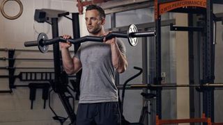 Man performs the reverse curl with an EZ-bar in a gym