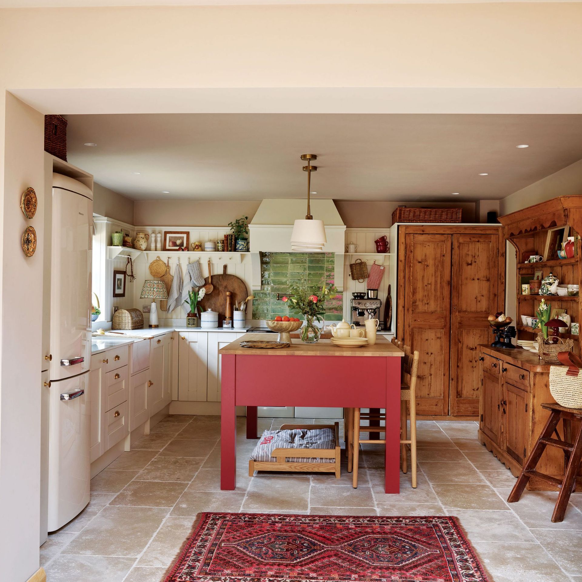 Country-style kitchen with cream cabinets and wooden accents, red island and bold rug
