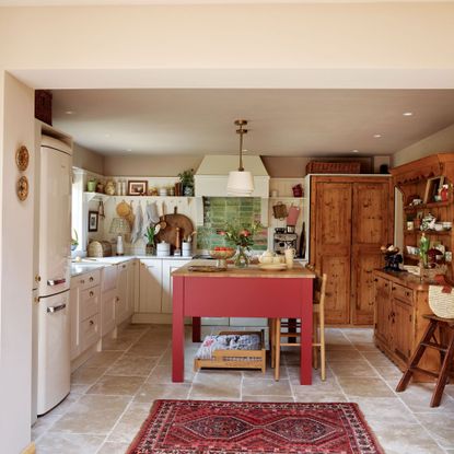 Country-style kitchen with cream cabinets and wooden accents, red island and bold rug