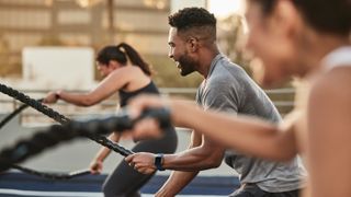 Group of happy people workout out outdoors using battle ropes