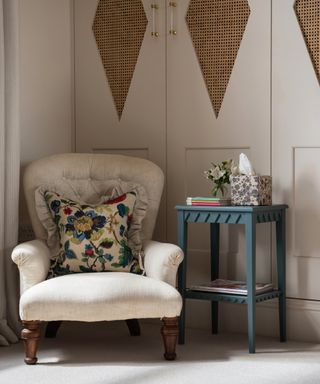 bedroom with fitted wardrobes in taupe, plain upholstered armchair with floral couch pillow, blue side table, Georgie Wykeham Designs