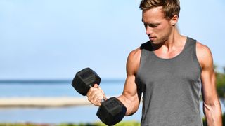 Man holding a dumbbell in right hand with elbow flexed during arm workout outdoors