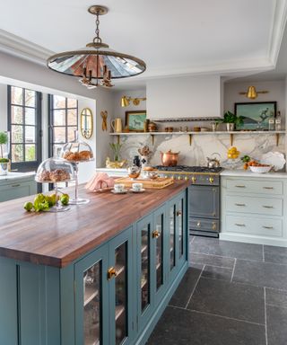A kitchen with a blue-green island, marble backsplash and large pendant light fitting