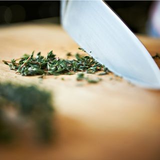 A close-up of a knife chopping thyme for christmas dinner