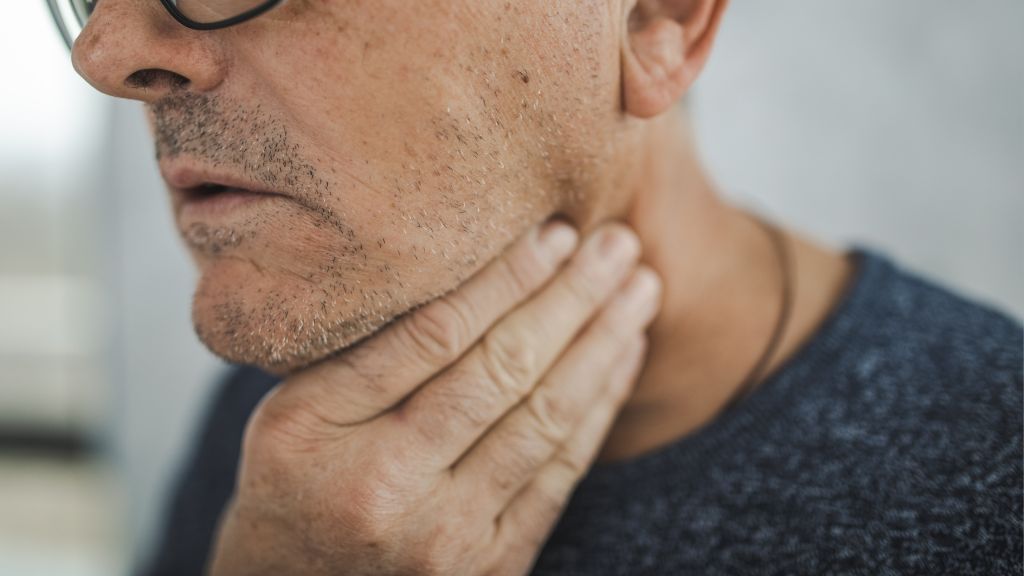 close up of an older man holding his throat in discomfort, as if it&#039;s sore