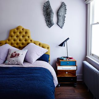 bedroom with chic bedding and bespoke mustard coloured headboard bedside cabinet and wings on wall