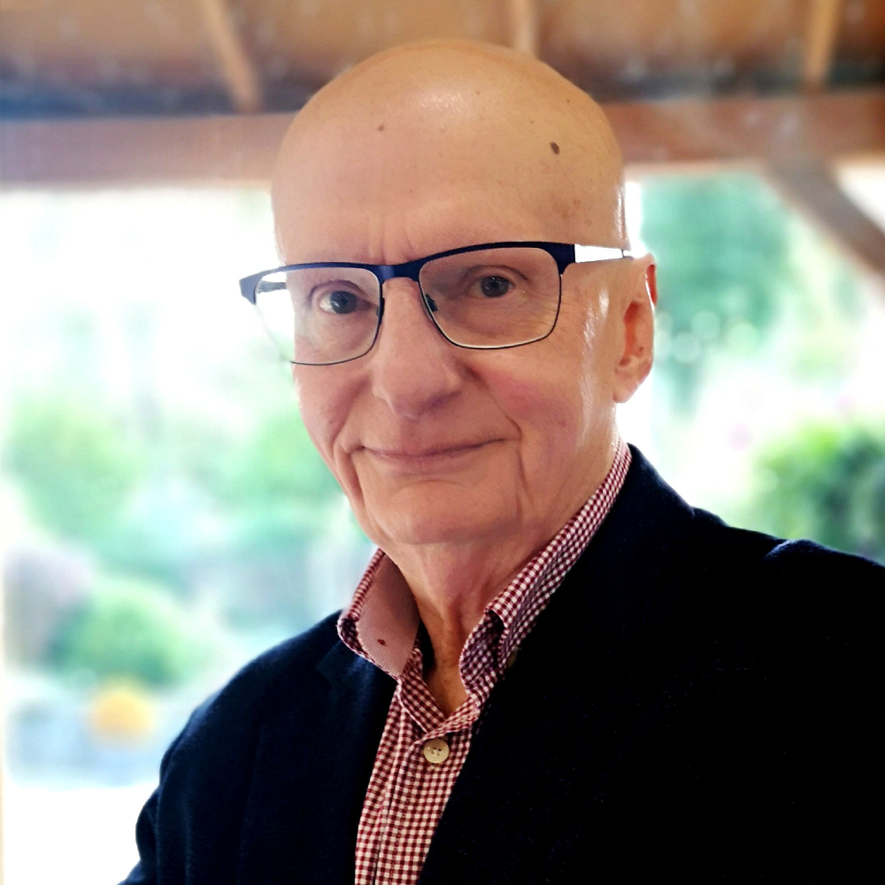 older male with no hair, glasses, wearing red check shirt and black jacket