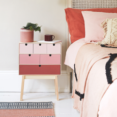 A set of pink drawers next to a bed with pink bedding.