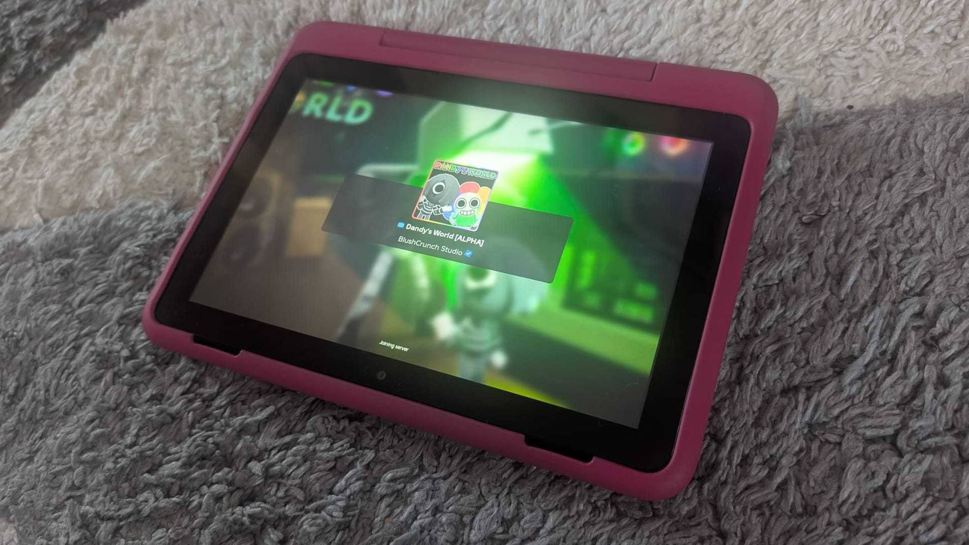 Fire HD 8 Kids Pro tablet on grey carpet with Roblox Dandy's World loading screen.