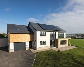 Exterior of house with white render, areas of timber cladding and dark grey doors and windows