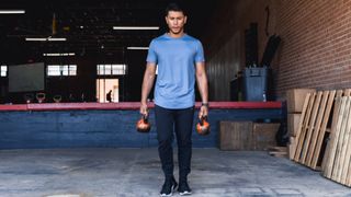 A man doing farmer carries with two kettlebell