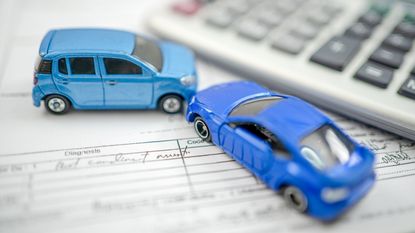 Two toy cars and parked hood to hood next to a calculator on top of insurance paperwork.