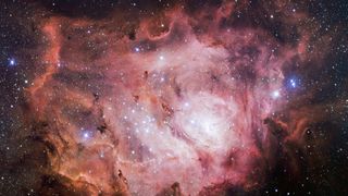 Swirls of pink and orange gas and dust form a brilliant glowing nebula amidst the stars in deep space
