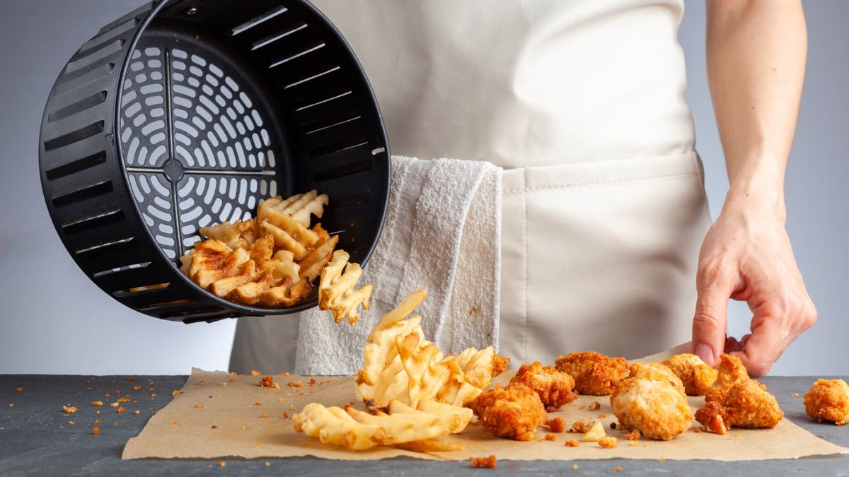 An air fryer basket tipping out waffle fries and chicken nuggets