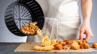 An air fryer basket tipping out waffle fries and chicken nuggets