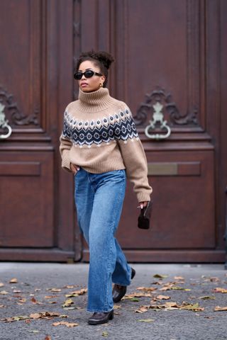 woman walking in the street in a fair isle sweater, jeans, and boots