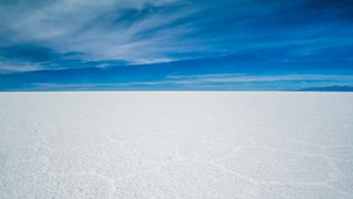 white salt flat in the foreground and a deep blue sky above with a few wispy white clouds.