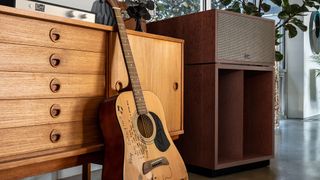 Klipsch La Scala AL6 speaker next to a wooden sideboard and an acoustic guitar. The guitar has handwriting on it saying "keep swinging" and some "rules of rock".