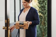 A woman retrieves an Amazon Pharmacy package that was just delivered at her front door.