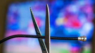 Scissors cutting a coaxial cable in front of a television