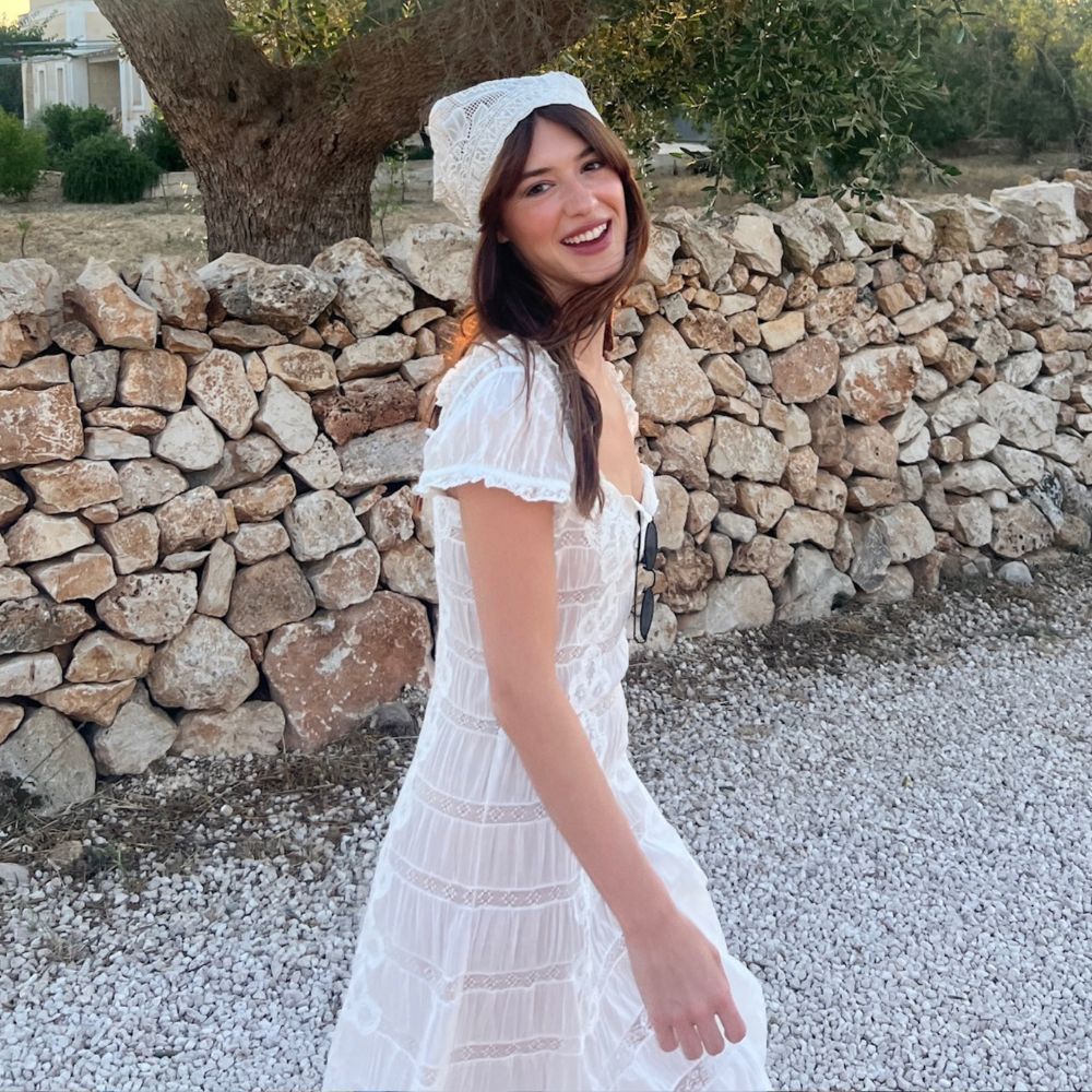 Daisy Edgar Jones wears a white midi dress with black flats, a white headscarf and a raffia bag.