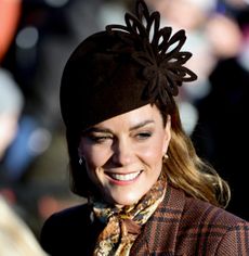 Princess Kate smiling, wearing a brown plaid coat and brown hat