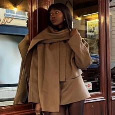 A photo of @emmanuelleuk in a brown co-ord and scarf outside a patisserie