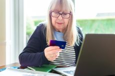 A retired woman looks concerned as she holds her credit card because she may have fallen victim to pension scams (image: Getty Images)