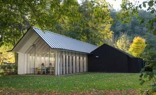 A photo of the Rievaulx Abbey Visitor Centre & Museum with a triangular wooden roof with glass windows and entrance. The building is surrounded by green trees.