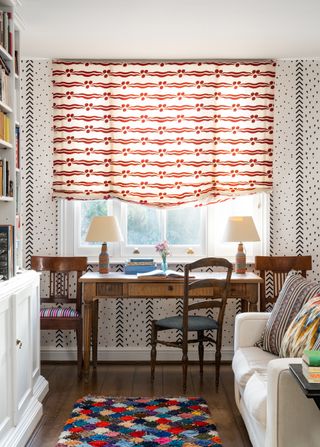 home office with wooden desk in front of a window and a semi-closed red and white roman blind