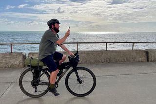 Tech Writer Matt Bikepacking along the South Coast of England, with the sea and sea wall behind him