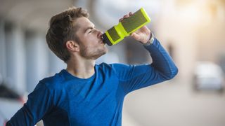 Young sporty runner drinking isotonic drink from a plastic drinks bottle