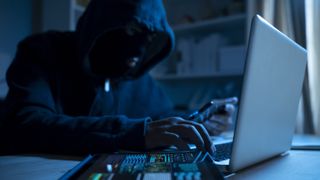 hacker in a hoody typing on a laptop