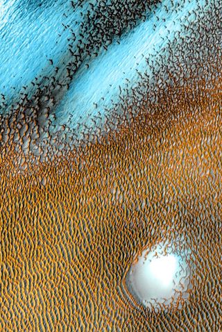 While it might look like a painting or a still from a science fiction film, this is actually an image of dunes on the surface of Mars. This image shows dark dunes surrounding Mars' northern polar cap. The scene is colorful, but these are false colors with cooler temperatures showing as blue and warmer areas seen as yellowish. The scene, created from images taken from 2002 to 2004 by the Mars Odyssey orbiter's thermal emission imaging system instrument, was released as part of a series of images celebrating Odyssey's 20th anniversary.