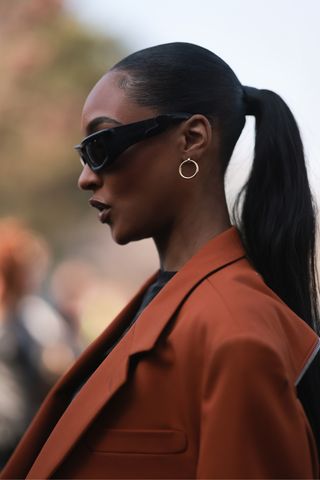 Jourdan Dunn is seen with a low ponytail, whilst wearing an orange brown blazer, black shirt, black sunglasses and golden earrings, outside Off White, during Pariser Fashion Week on March 02, 2023 in Paris, France.