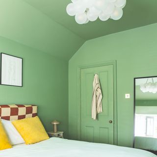 A green colour-drenched bedroom with a chequerboard headboard and yellow cushions on the bed