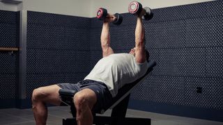 Man performs hammer chest press on weights bench set to an incline in a gym